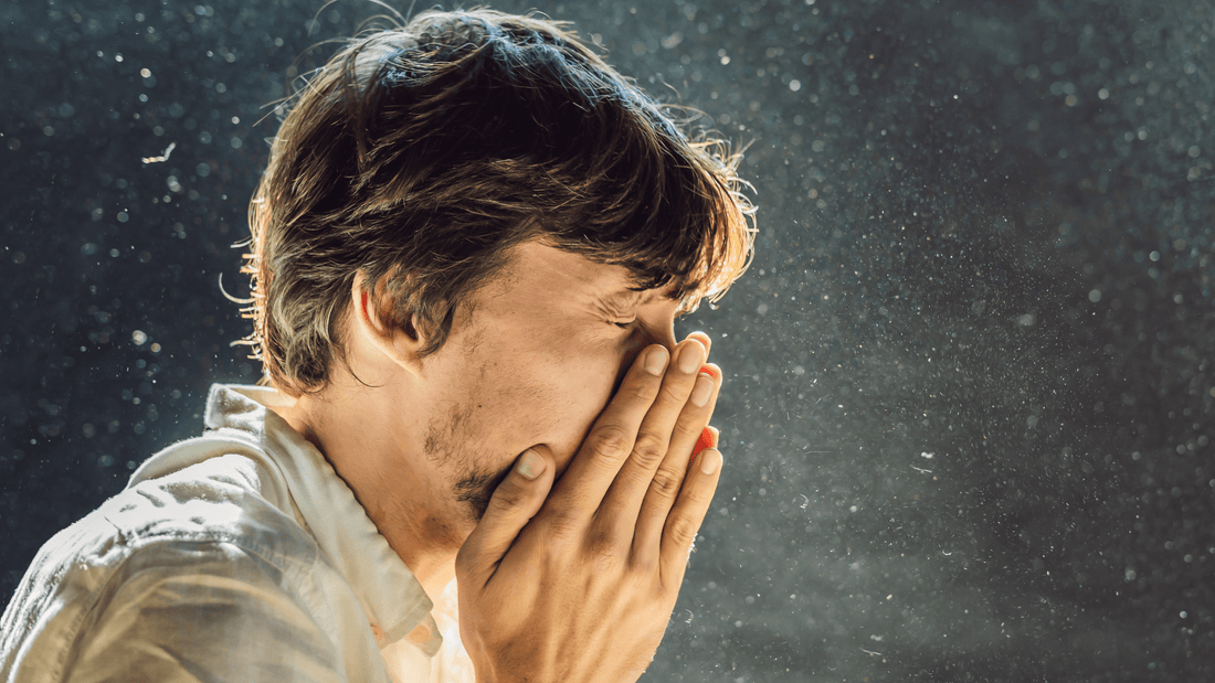 Mann der in einer Staubwolke steht und sich die Hände beim Nießen vor sein Gesicht hält