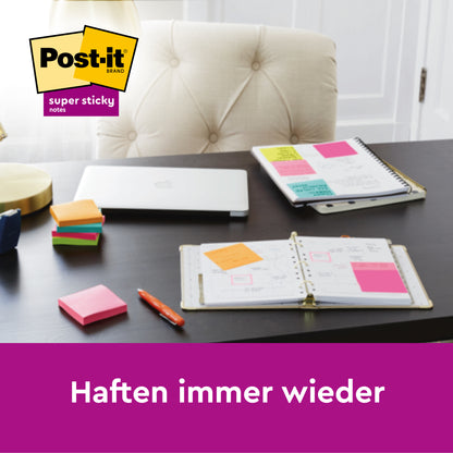 Ein Schreibtisch mit einem geschlossenen Laptop, offenen Planern, Stiften und Stapeln von blauen Post-it® Super Sticky Z-Notes in einem weißen Bärenspender (76 mm x 76 mm, 45 Blatt/Block, 2 Blöcke/Packung) von 3M Deutschland GmbH. Das Post-it-Logo befindet sich oben links; der deutsche Text lautet: "Haften immer wieder.