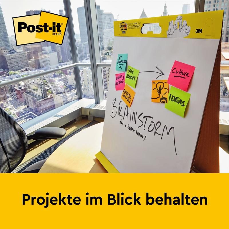 V kanceláři s výhledem na město stojí 3M Post-it® Super Sticky samolepicí schůzkový graf/flipchart s podstavcem (58,4x50,8 cm, 20 listů/blok) - ideální pro poznámky jako "Navrhujeme", "Uchovat prostory" a další. Udržujte projekty na dohled.