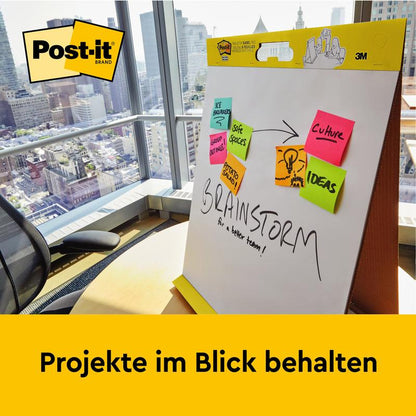 V kanceláři s výhledem na město stojí 3M Post-it® Super Sticky samolepicí schůzkový graf/flipchart s podstavcem (58,4x50,8 cm, 20 listů/blok) - ideální pro poznámky jako "Navrhujeme", "Uchovat prostory" a další. Udržujte projekty na dohled.