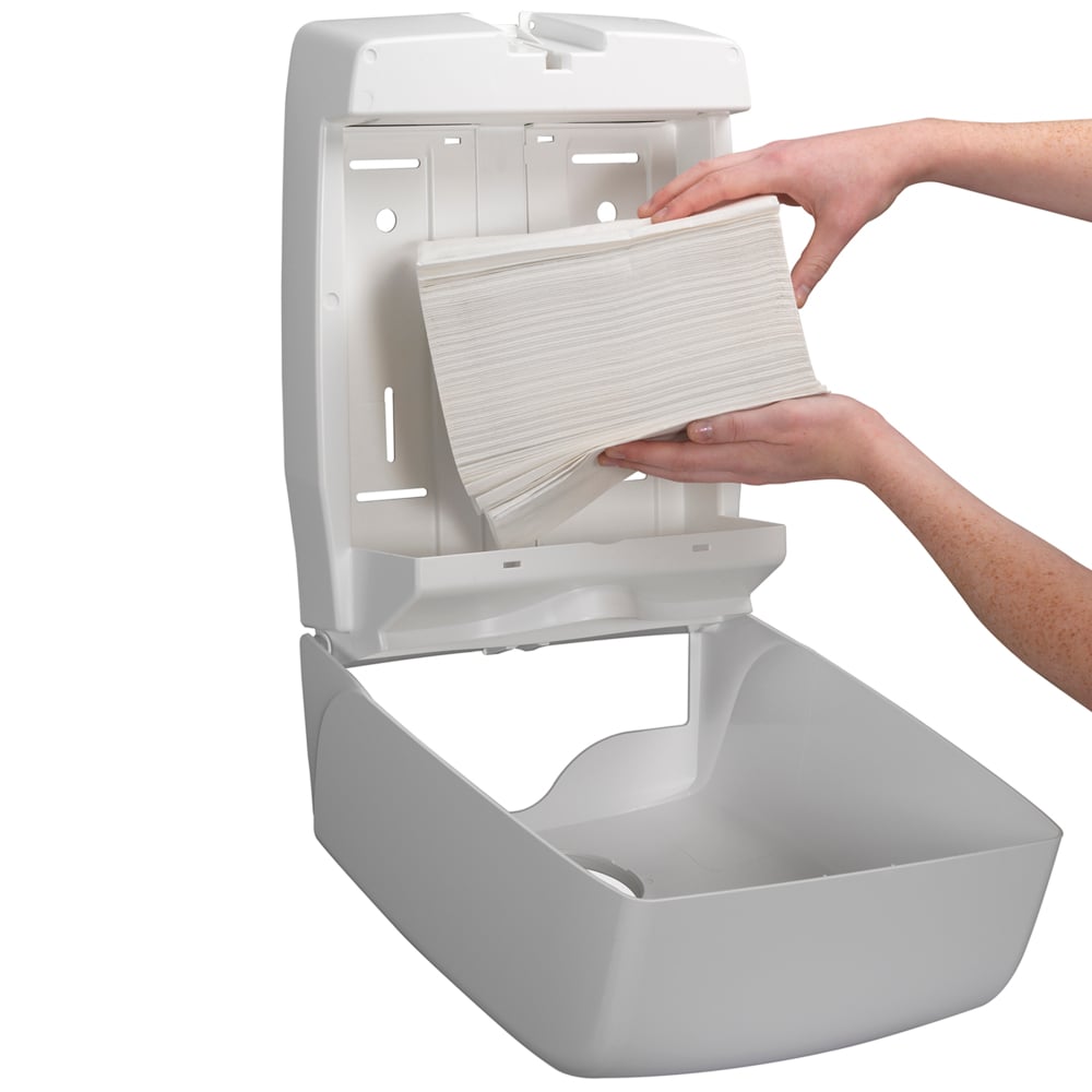 Osoba doplňuje na stěnu namontovaný dávkovač Kleenex® Ultra™ skládanými ručníky Interfold Bílý (15 klipů x 96 listů) od Kimberly-Clark GmbH a zajišťuje hygienické sušení rukou, protože otevřený dávkovač umožňuje snadné doplňování.