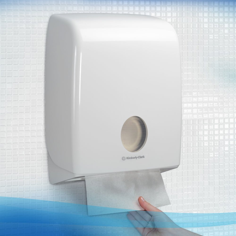 Ruka vytahuje ručník Scott® - MultiFold / Bílá z nástěnného dávkovače od Kimberly-Clark GmbH v obložené koupelně a zajišťuje tak hygienické sušení rukou.