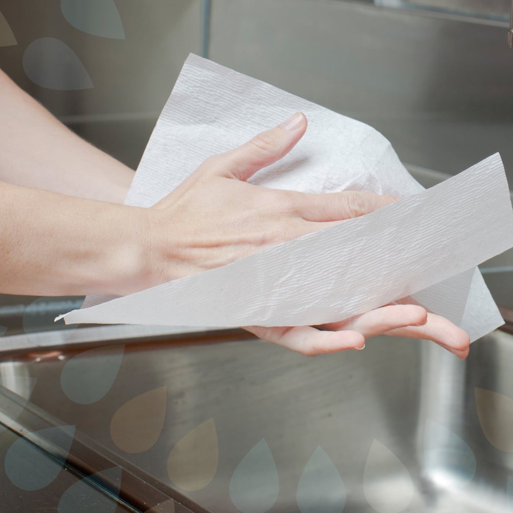 Někdo si suší hygienické ruce s Kleenex® Ultra™ ručníky - Interfold, bílá, střední (70 kusů, Kimberly-Clark GmbH) nad umyvadlem, v pozadí je vidět část kohoutku.