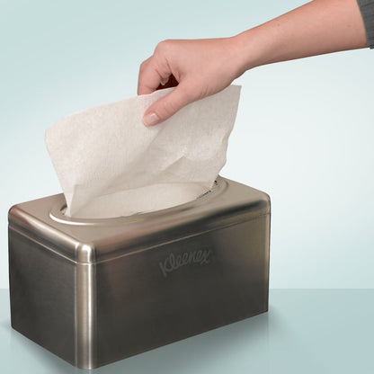 Eine Hand zieht ein Taschentuch aus einem Kimberly-Clark GmbH Kleenex® Handtuchspender aus Edelstahl - Zupfbox/klein, verchromt (2 Spenderboxen/Karton), der auf einer hellblauen Fläche steht.