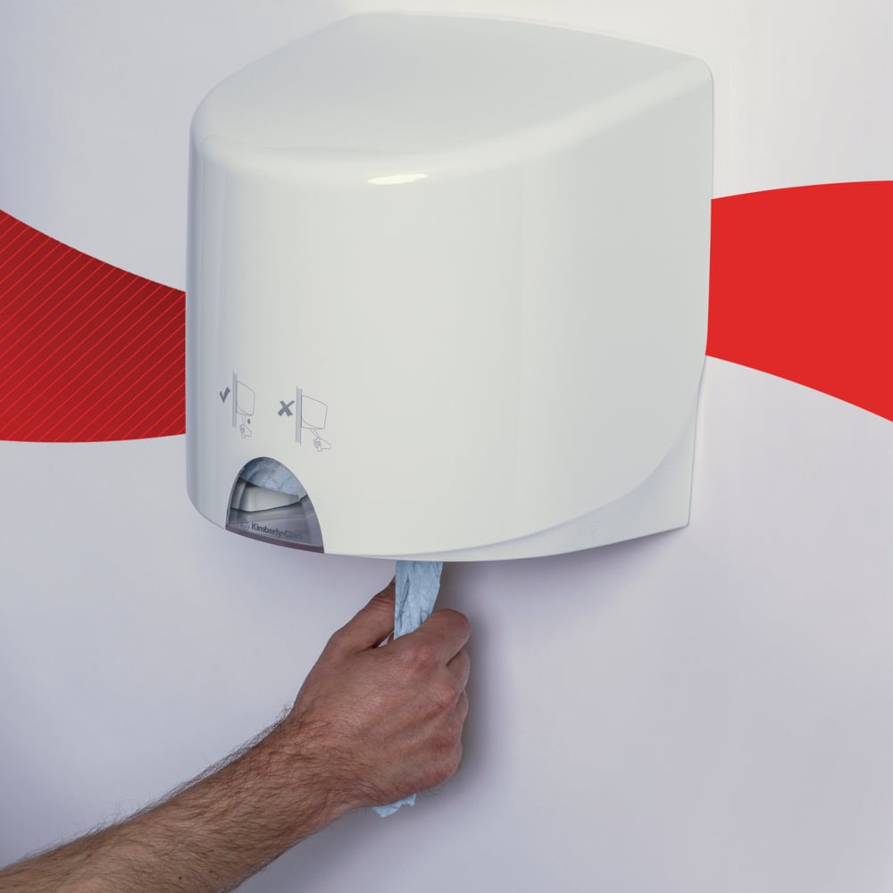 Ruka vytahuje modrou papírovou utěrku WypAll® L10 pro potraviny a hygienu od Kimberly-Clark GmbH z bílého nástěnného zásobníku před bílou zdí s červeným vlnovým pruhem.