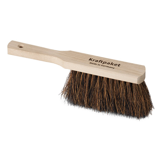 Der Nölle Profi Brush Handfeger 30 cm von Nölle Profi Brush Bürsten- & Pinseltechnik e.K. hat einen hellen Holzstiel mit "Kraftpaket Made in Germany", dichte dunkle Borsten aus Arenga- und Kokosfasern und ein Loch zum Aufhängen.