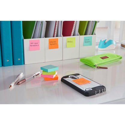 Uklizený stůl se zeleným penálem, tužkami, 3M Post-it® Super Sticky Notes (47,6 x 47,6 mm, 90 listů, 100 % PEFC), smartphonem s popsanou poznámkou, pořadači pro kancelářské potřeby a zprávy a modrým držákem na lepicí pásku v pozadí.
