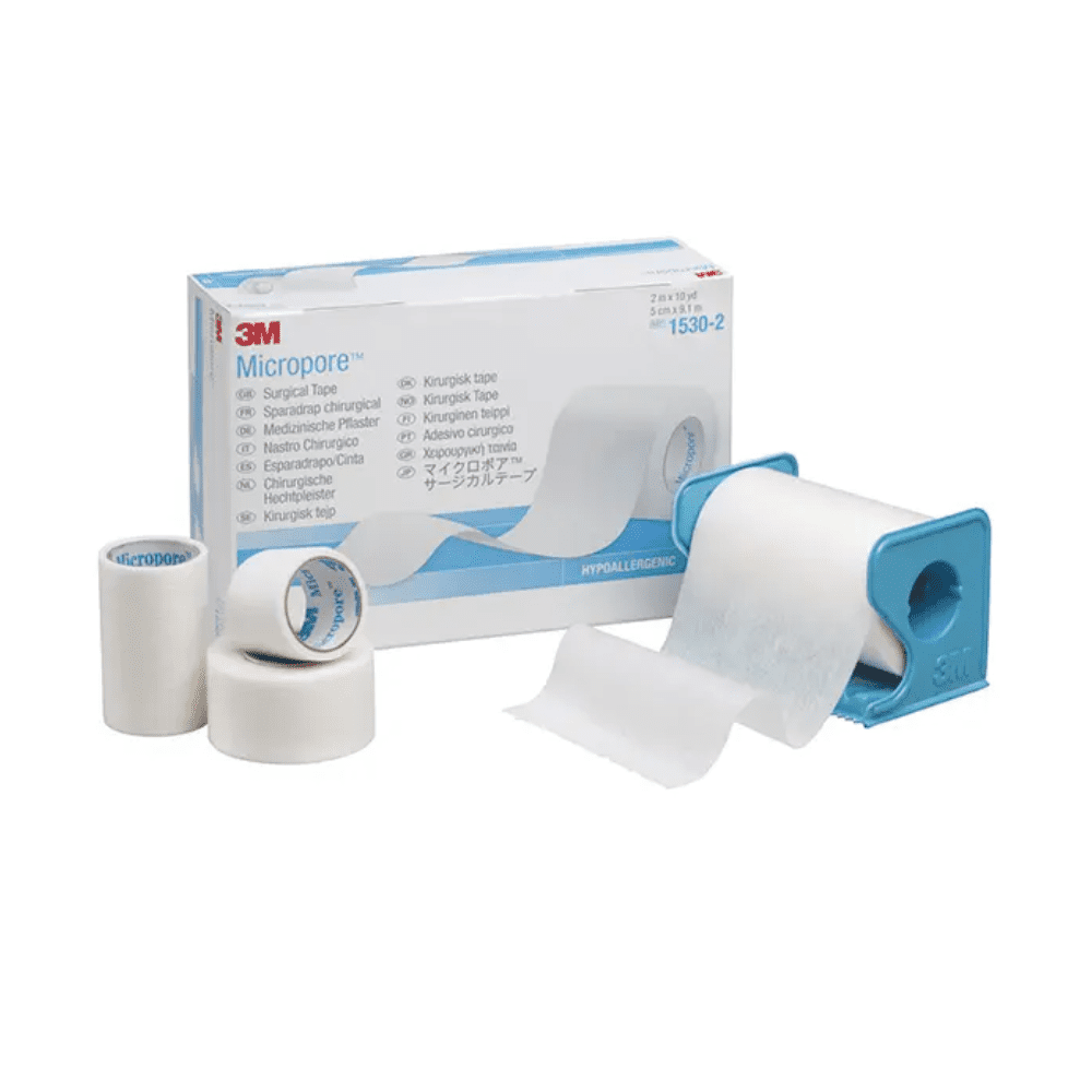 Obrázek ukazuje 3M Healthcare Germany GmbH 3M-Medica Micropore náplast, tělová barva – 12 kusů | Balení (12 kusů)-Krabička s náplastmi různých velikostí před ní. Jedna náplastová role je v modrém zásobníku, zatímco další dvě náplastové role a jedna menší role stojí vzpřímeně vedle krabičky. Hypoalergenní náplast je bílá.