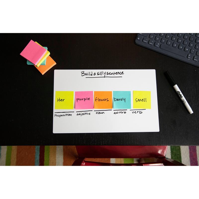 Na černém stole stojí tabule s nápisem "Vytvořte hloupou větu". Kostky Post-it® Notes v ultra barvách, 76x76 mm, od 3M Deutschland GmbH ukazují slovní druhy. Dále na stole: suchý fix, poznámkový blok a klávesnice.