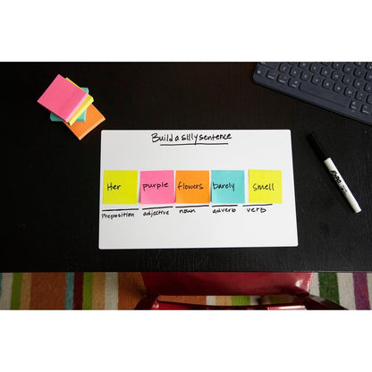 Na černém stole stojí tabule s nápisem "Vytvořte hloupou větu". Kostky Post-it® Notes v ultra barvách, 76x76 mm, od 3M Deutschland GmbH ukazují slovní druhy. Dále na stole: suchý fix, poznámkový blok a klávesnice.
