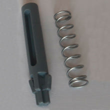 Na světlém pozadí je vyobrazena kovová pružina a tmavě šedý válcový náhradní dveřní čep s drážkami a zuby, část DI Protect dveřního čepu a pružiny (1 kus) od Diversey Deutschland GmbH & Co. OHG, které ukazují robustní materiály pro DI Protect vozík.