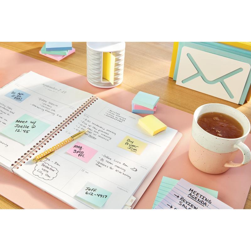 Otevřený plánovač s ručně psanými poznámkami leží na stole vedle šálku čaje, kartiček, pera a poznámkových bloků Post-it® Notes v žluté barvě (38 mm x 51 mm, 3M Deutschland GmbH) a kontejneru.
