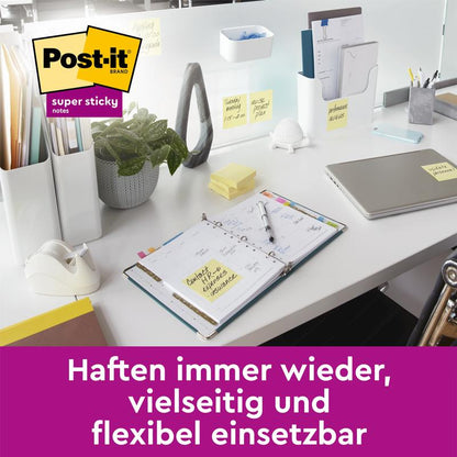 Na moderním kancelářském stole jsou Post-it® Super Sticky Notes, žluté (76x127 mm, 90 listů/blok, 14+2 volné bloky/balení) od 3M Deutschland GmbH připevněny na různých površích. Logo Post-it se objevuje vlevo nahoře a německý text dole.