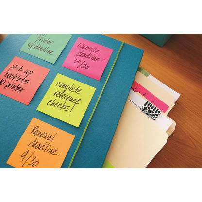 Modrá složka s barevnými kostkami Post-it® Notes v ultra barvách od 3M Deutschland GmbH (76x76 mm, 450 listů/blok, PEFC certifikováno), ve které jsou uvedeny úkoly, leží vedle manilových složek a poznámkového bloku na dřevěném stole.