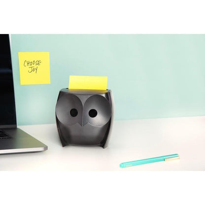 Černý dávkovač Post-it® Z-Notes "Sova" (3M Deutschland GmbH) se žlutými Super Sticky Z-Notes stojí na bílém stole, vedle laptop a modrá tužka. Na zdi visí lístek "CHOOSE JOY" před světle modrým pozadím.