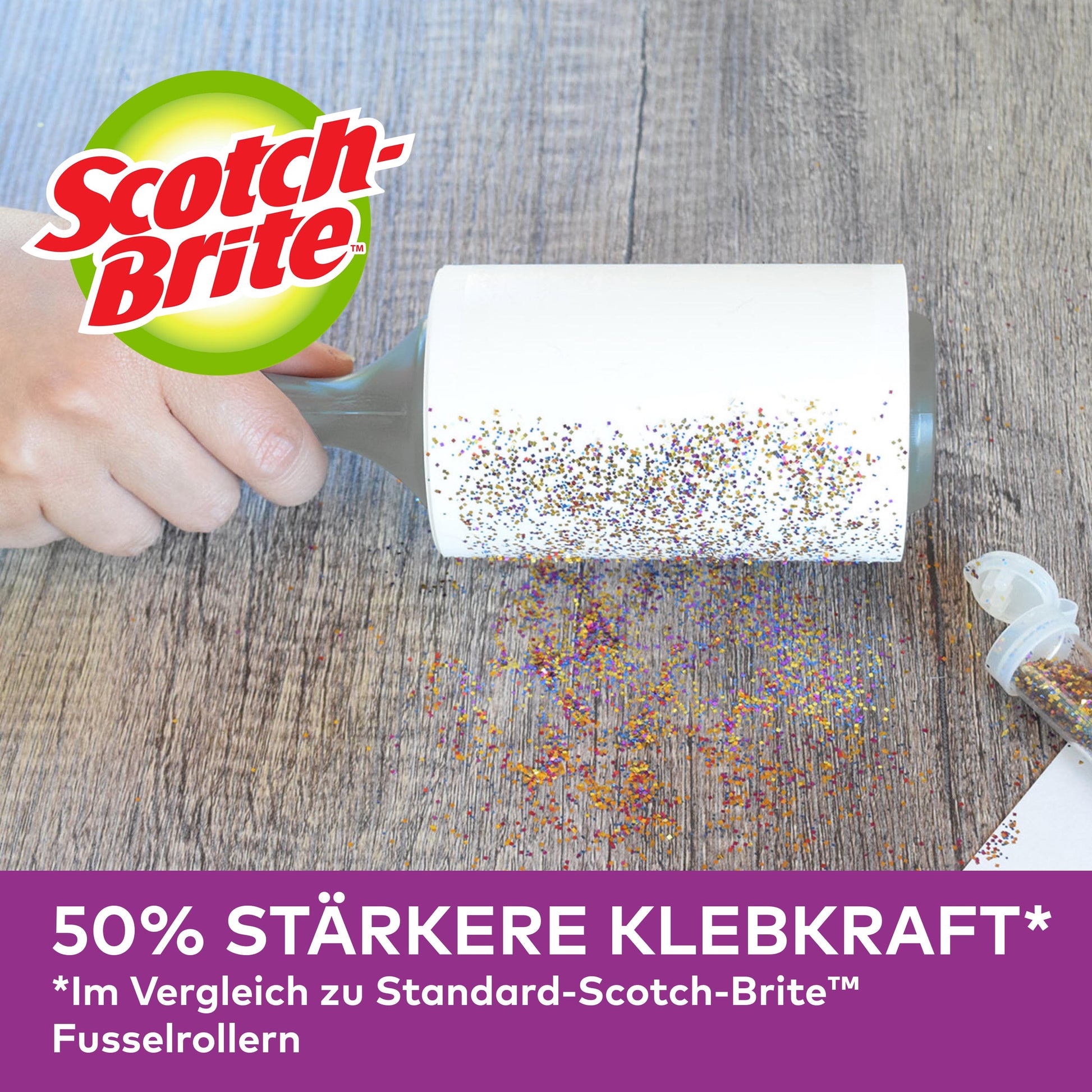 Eine Hand benutzt eine Scotch-Brite™ Pet Extra Sticky* Ersatzrolle für Tierhaare (48 Blatt, 1 Pack) von 3M Deutschland GmbH, um verschütteten Glitter von einer Holzoberfläche aufzunehmen. Der Text unten wirbt mit 50% stärkerer Klebekraft. Ein offener Glitzerbehälter ist in der Nähe.