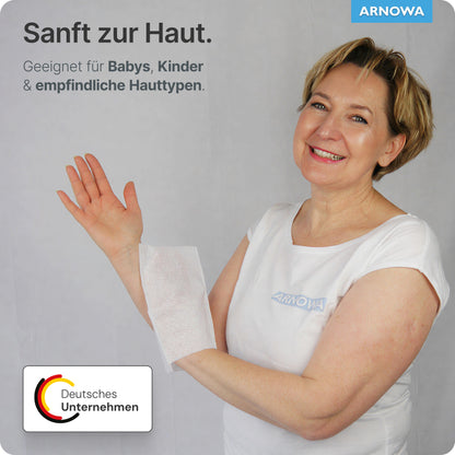 Eine Frau in einem weißen Hemd lächelt, während sie einen ARNOMED Einmalwaschhandschuh Spunlace mit PE, wasserabweisend (Beutel, 50 Stück) der ARNOWA GmbH über den Arm hält. Der deutsche Text hebt die sanfte Pflege für Babys, Kinder und empfindliche Haut hervor.