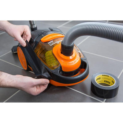 Osoba opravuje prasklé oranžovo-černé pouzdro vysavače pomocí univerzální lepicí pásky Scotch® Extremium™ (3 m x 19 mm) od 3M Deutschland GmbH, přičemž role leží na šedé dlažbě v blízkosti.