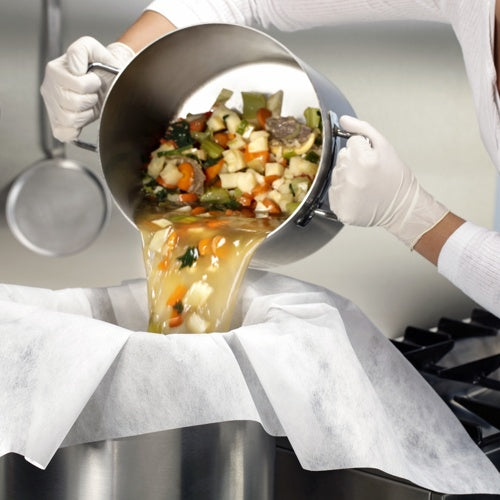 Někdo v bílých rukavicích nalévá zeleninu a vývar přes pergamenem vyložené síta a filtrační utěrky (100x100 cm, 10 kusů) od Starpak do velké kovové nádoby a demonstruje tak praktické použití v kuchyni.