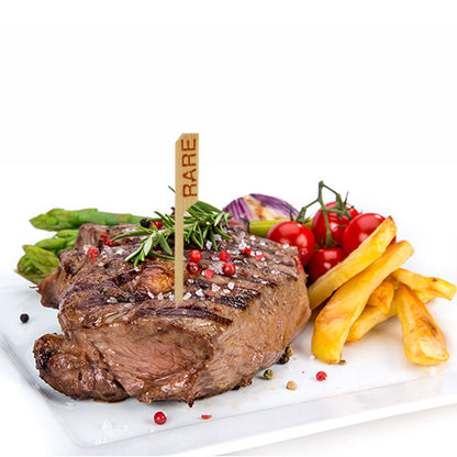 Grilovaný krvavý steak, označený steakovou značkou PAPSTAR 250 (9 cm) od PAPSTAR GmbH, podávaný s hranolky, chřestem, cherry rajčaty na větvičce, červenou cibulí a ozdobený rozmarýnem a pepřovými zrny – v restaurančním stylu.