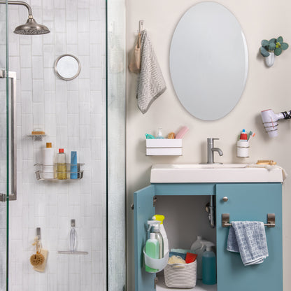 Ein Badezimmer mit einer Glasdusche auf der linken Seite, einem blauen Waschtisch, einem weißen Waschbecken, einem ovalen Spiegel und organisierten Toilettenartikeln. Handtücher hängen ordentlich am 3M Command™ Großer Badezimmer-Doppelhaken Nickel satiniert von 3M Deutschland GmbH nebenan.