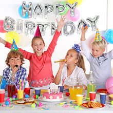 Čtyři děti s party čepičkami slaví narozeniny u ozdobeného stolu s dortem a party potřebami. Za nimi zdobí stěnu fóliové balónkové sety „Happy Birthday“ společnosti PAPSTAR GmbH ve stříbrné a pestrobarevné balónky.
