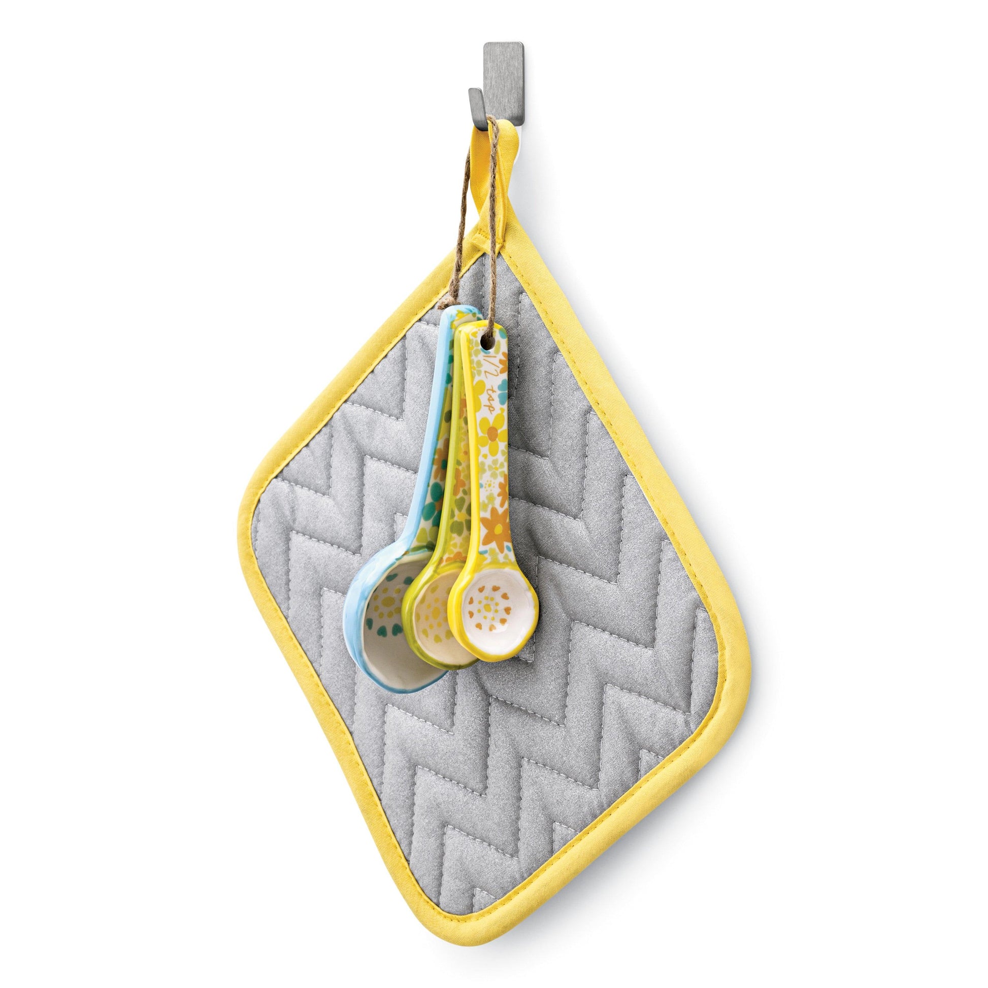 An einem Command™ Edelstahl-Metallhaken (Größe S) der 3M Deutschland GmbH hängt ein grauer, gesteppter Topflappen mit gelber Verzierung. Drei florale Messlöffel aus Keramik baumeln an einer braunen Schnur, die am Topflappen befestigt ist.