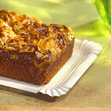 Auf dem PAPSTAR Papp-Teller eckig 13x20 cm, weiß, "pure" für Feste (12 Stück) der PAPSTAR GmbH ruht ein rechteckiger Kuchen mit gehobelten Mandeln - eine umweltfreundliche, elegante Serviermöglichkeit auf einer hellen Oberfläche mit grünem Glas dahinter.