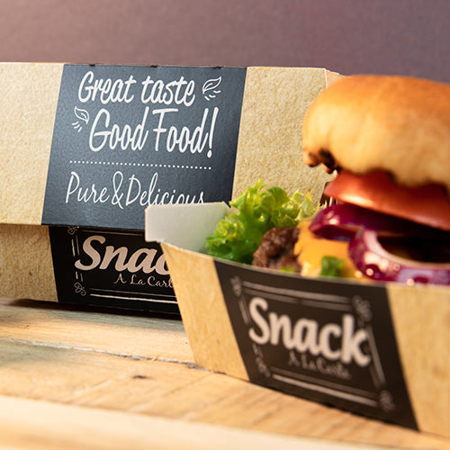 Papírový tácek s nápisem "Snack A La Carte" obsahuje hamburger se salátem, rajčetem a cibulí. V pozadí stojí PAPSTAR 50 burgerových krabic, karton "pure" "Good Food" od PAPSTAR GmbH: Dobrý chuť, Good Food! Čisté & lahodné.