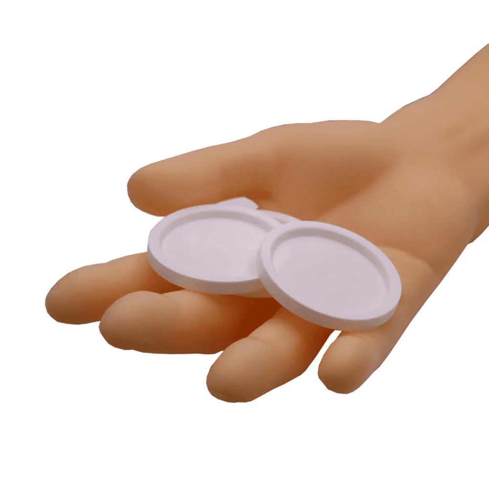 Jedna ruka drží dva kulaté AMPri víčka pro lékařské kelímky, bílé objekty před jednoduchým bílým pozadím.