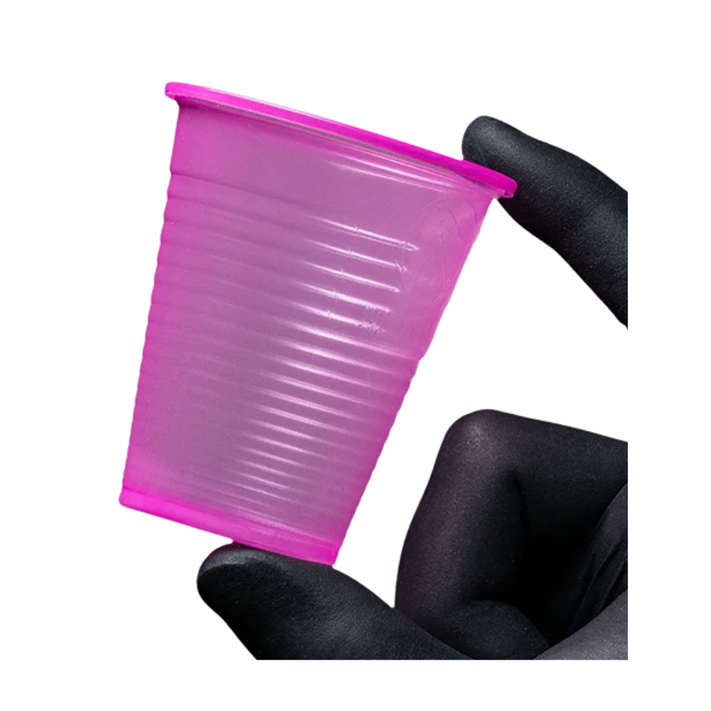 Malý růžový AMPri Dental PP ústní kelímek z polypropylenu je držen mezi dvěma rukavicemi pokrytými prsty před bílým pozadím. Tento jednorázový ústní kelímek od AMPri Handelsgesellschaft mbH, který je často k vidění v zubních ordinacích, má strukturovaný povrch s horizontálními drážkami.