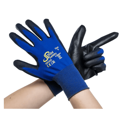 Pár zkřížených paží s ultralehkými modrými a černými bezpečnostními rukavicemi AMPri SolidSafety Tough Fine Touch vyzařuje prémiovou kvalitu. Otevřená dlaň levé rukavice směřuje dopředu, zatímco pravá má tvar prstové pistole. Tyto rukavice hrdě ukazují logo AMPri Handelsgesellschaft mbH a informace o velikostech od XS po XXL, což zajišťuje spolehlivý výkon.