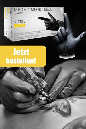 Eine tätowierende Person trägt schwarze Einweghandschuhe und arbeitet an einem Tattoo auf der Haut eines Kunden. Oben im Bild ist eine Verpackung der „MED-COMFORT Black Vitril“-Handschuhe von AMPri zu sehen. In der Mitte steht in einem gelben Feld der Text „Jetzt bestellen!“.
