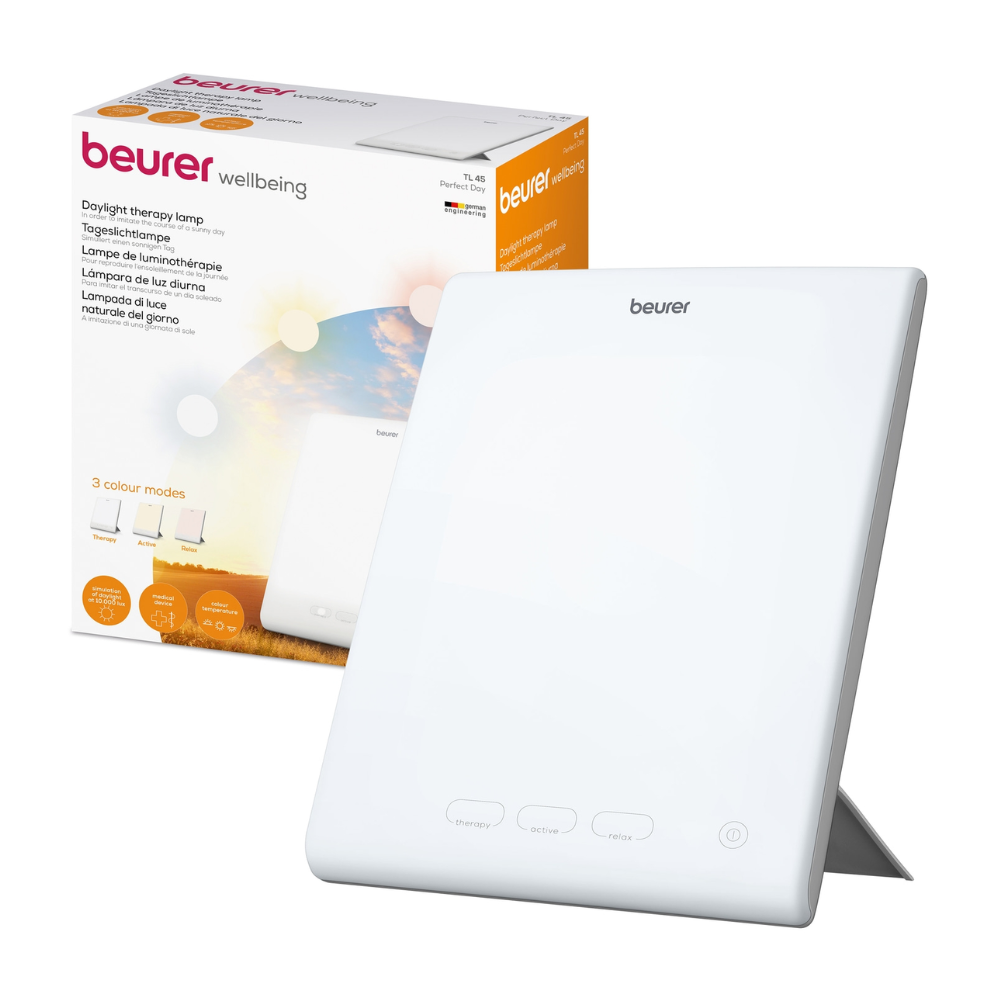 Bílá Beurer Perfect Day denní lampa TL 45 od Beurer GmbH je zobrazena vedle svého obalu. Na obalu je název produktu a popis v několika jazycích, přičemž jsou zobrazeny různé režimy barevné teploty. Lampa má jednoduchý design s tlačítky na přední straně, díky čemuž je ideální pro regulaci vašeho denního a nočního rytmu.