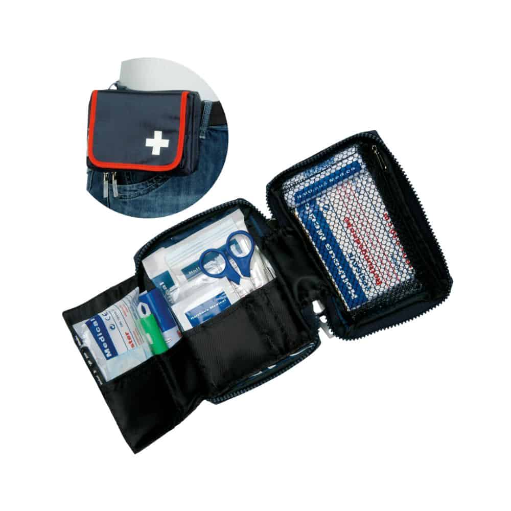 Otevřená lékárnička Holthaus Medical TRAVEL modrá/červená od společnosti Holthaus Medical GmbH & Co. KG je zobrazena s lékařským materiálem, jako jsou obvazy, nůžky a antiseptické ubrousky. Obal je opatřen symbolem bílého kříže a upevněním na opasek. Vložený obrázek ukazuje sadu připevněnou k džínovému opasku.
