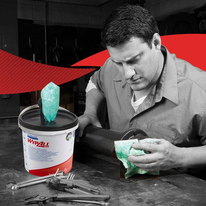 Muž v pracovním oblečení čistí kovovou trubku zelenou utěrkou WypAll® od Kimberly-Clark GmbH. Krabice (6 dávkovačů) utěrek leží mezi nástroji. Fotografie je převážně černobílá, kromě utěrek a etikety.