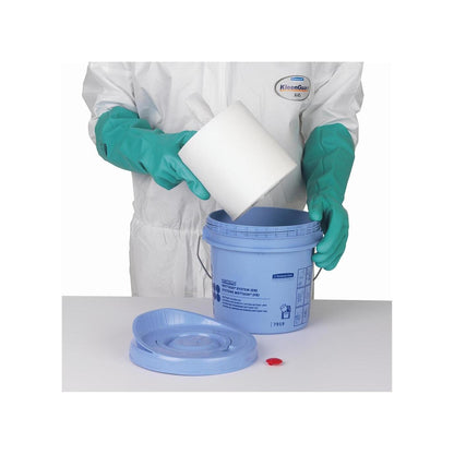Osoba v zelených rukavicích a bílém obleku vkládá roli utěrek Kimtech® Wettask™ do modrého zásobníku na utěrky od společnosti Kimberly-Clark GmbH; víko a červený uzávěr leží na stole vedle.