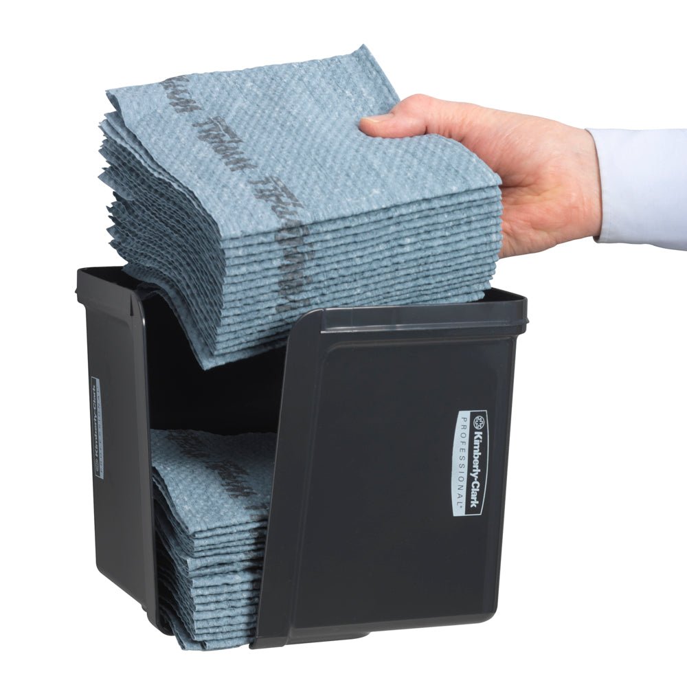 Ruka vkládá čtvrtinově složené ubrousky do šedého dávkovače Kimberly-Clark Professional™ od Kimberly-Clark GmbH - pro hygienické vyjmutí ubrousků. Úhledně složené ubrousky a přední etiketa jsou viditelné.
