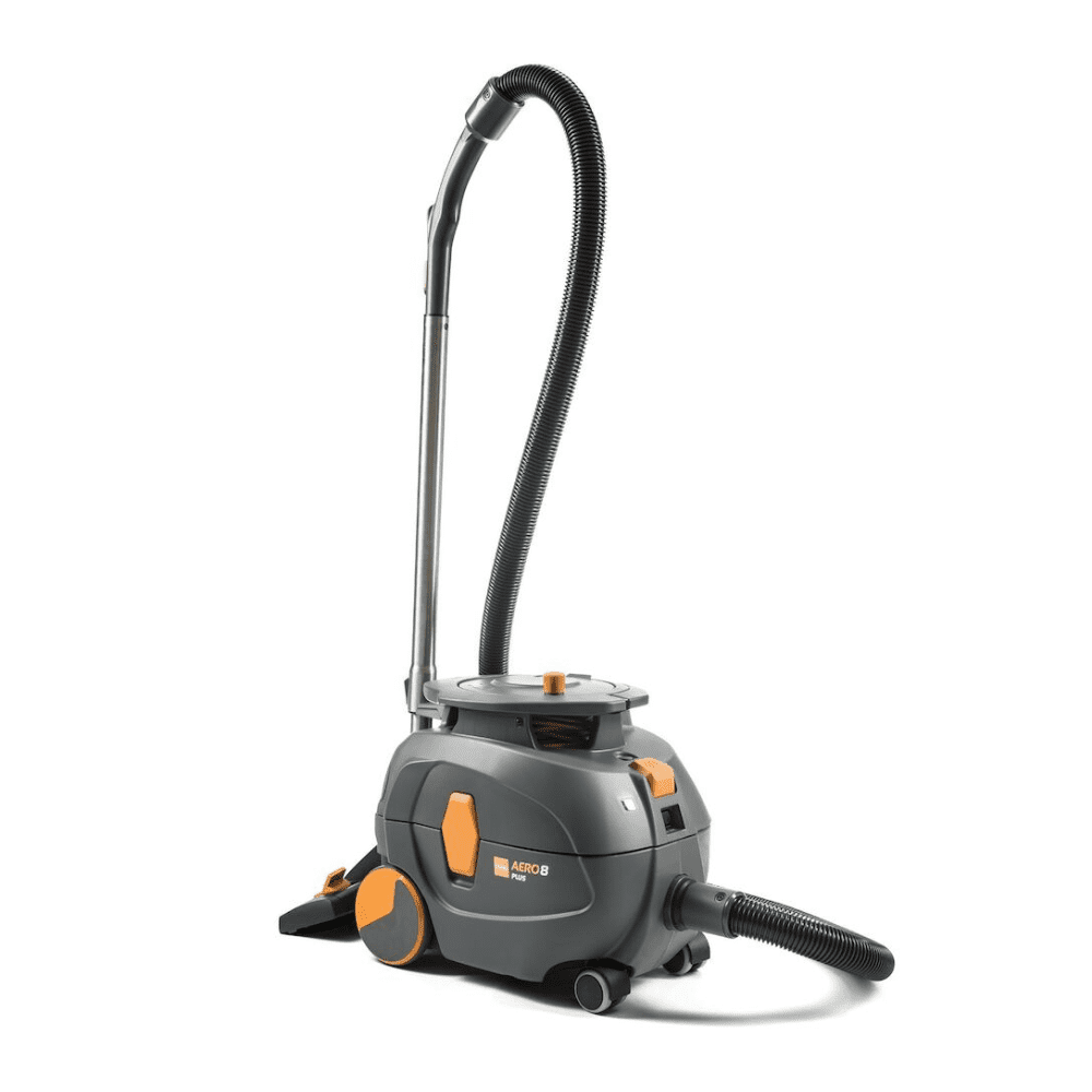 Vysavač TASKI AERO 8 PLUS, poskytovaný společností Diversey Deutschland GmbH & Co. OHG, v šedé a oranžové barvě, stojí vzpřímeně. Tento kompaktní a výkonný vysavač má dlouhou flexibilní hadici a válcovité tělo s velkými zadními koly a menšími předními koly pro vynikající mobilitu a efektivní čištění. Jeho provoz je vylepšen technologií šeptání pro tichý provoz.