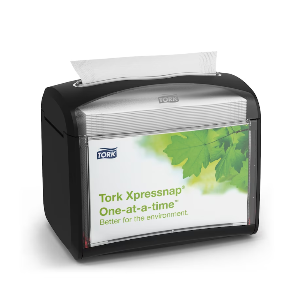 Černý stolní dávkovač ubrousků Tork Xpressnap® 272611, distribuovaný společností TORK – Essity Professional Hygiene Germany GmbH, je prezentován s etiketou se zelenými listy a zprávou „Jednotlivě. Lepší pro životní prostředí“. Jeden ubrousek je částečně vydáván shora, aby se podpořila hygiena a efektivní spotřeba ubrousků.