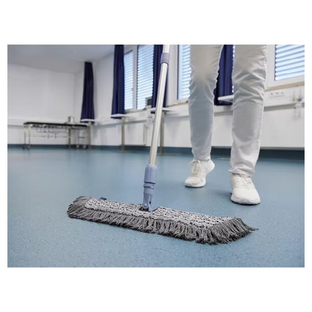 Eine Person in weißen Schuhen und Hosen wischt mit einem Vileda GmbH Professional Swep Duo r-MicroCombi Mop - 50 cm einen blauen Boden in einem Raum mit geschlossenen Jalousien und blauen Vorhängen. In der Nähe stehen ein Klapptisch und unter den Fenstern ein Heizkörper.