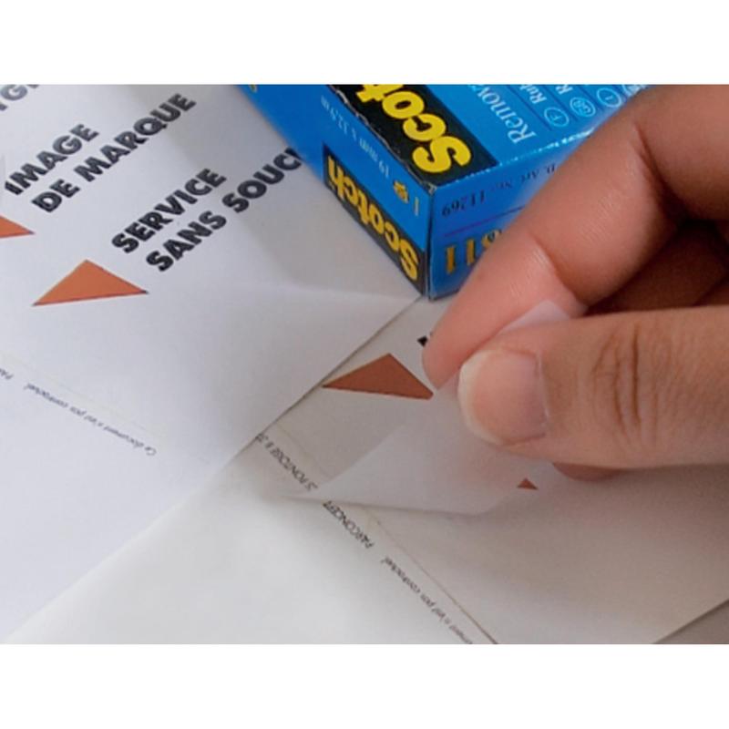 Ruka odtrhává trojúhelníkovou nálepku z listu s nápisem "IMAGE DE MARQUE SERVICE SANS SOUCI", zatímco v pozadí stojí krabička Scotch® neviditelné lepicí pásky od 3M Deutschland GmbH, odnímatelná, 19 mm x 33 m, 1 role | 1 kus.
