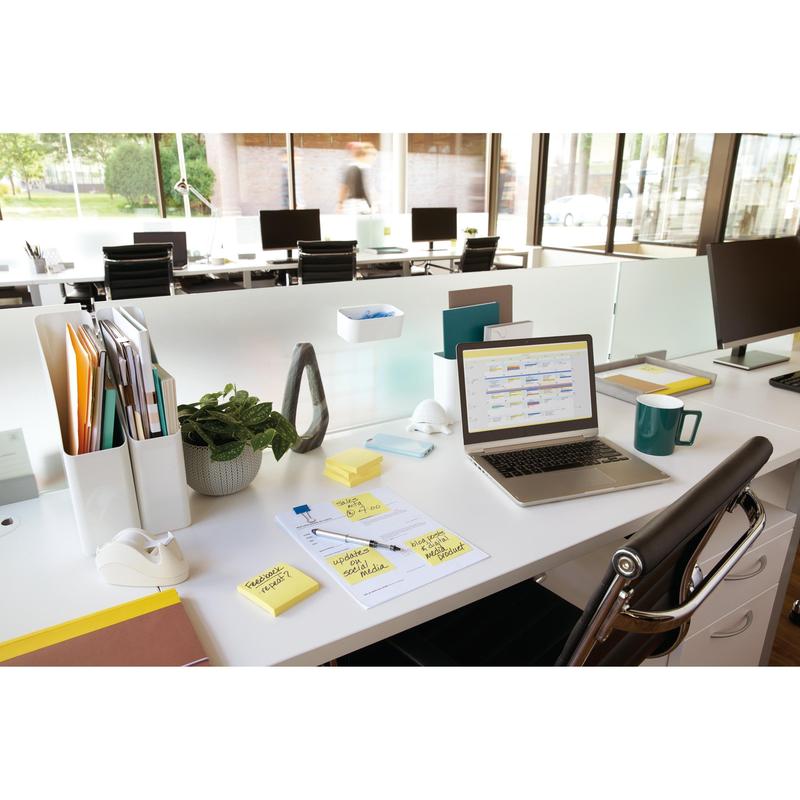 Moderní kancelář s laptopem, žlutými Post-it® Notes od 3M (76x76 mm, 100 listů/blok), šálkem, dokumenty, rostlinami a příslušenstvím na bílém stole. V pozadí jsou vidět další stoly a velká okna.