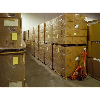 Ve skladu jsou stohy Post-it® Super Sticky Notes ve velkém formátu, Ultra Žlutá (101 x 152 mm, 90 listů/blok, 6 bloků), od 3M Deutschland GmbH, zabalené na paletách. Vedle stojí červený ruční paletový vozík.