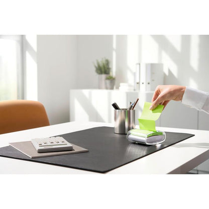 Osoba vytahuje žlutou Post-it® Super Sticky Z-Note (76 x 76 mm) z černého PRO Post-it® Z-Notes Dispenser od 3M Deutschland GmbH, na uklizeném psacím stole s kalkulačkou, držákem na pera a černou podložkou za jasného denního světla.